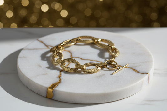 Gold chain bracelet on a marble coaster with a blurred gold background