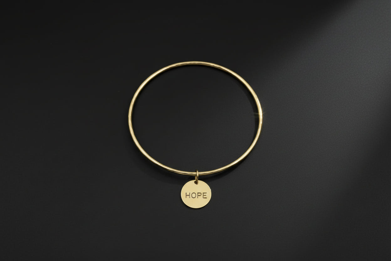 Gold bracelet with a 'HOPE' tag on a black background