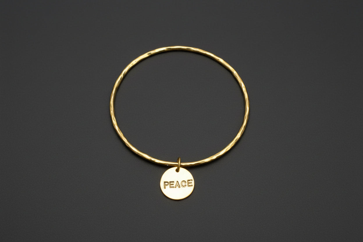 Gold bracelet with a 'PEACE' tag on a black background