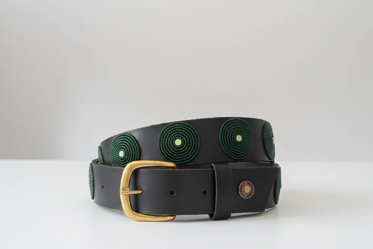 Black belt with green circular patterns and a gold buckle on a white surface.